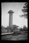 1987-2788 Een dame zit op een bankje aan de centrale vijver in Diergaarde Blijdorp. Op de achtergrond de uitkijktoren ...