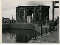 V-169-21-01-1 Mensen wandelen langs de restanten van de Delftsche Poort na het bombardement van mei 1940. Rechts is de ...