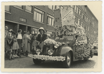 WN-186 Bloemencorso door de stad. Een met bloemen versierde auto met reclame voor het Rotterdamsche Parool rijdt langs ...