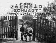 1977-3206 Drie jongens staan met hun opgerolde handdoek bij het hek van Stichting Zwembad Schuagt te Krimpen a/d Lek - ...