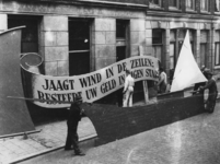 1977-3522 Bij het stadhuis wordt gewerkt aan een model van een zeilschip met het opschrift: Jaagt wind in de zeilen: ...
