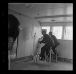 5592 Twee mannen in pak trainen op een oefenfiets (spinning) in de sportruimte van passagiersschip Nieuw Amsterdam. ...