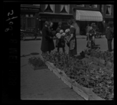 5708 Op de Rechter Rottekade laat een verkoopster bloemen zien aan klanten op een bloemen- en plantenmarkt. Rechts ...
