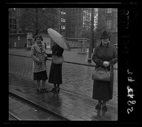 5862 Drie vrouwen wachten op de Coolsingel in de regen op de tram. Een vrouw draagt een paraplu, een andere vrouw houdt ...