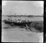 THO-1065 Een woonboot ligt afgemeerd bij de Schaardijk. Op de voorgrond een zandhoop tijdens de renovatie van de dijk. ...