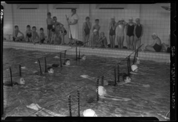 THO-1148 Tijdens een zwemles zwemmen leerlingen door poortjes. Uit een serie over schoolzwemmen in het Sportfondsenbad ...