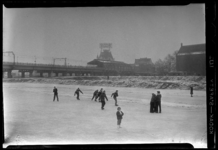 THO-1181 Schaatsers schaatsen tussen de Hoogstraat en de Vissersdijk. Op de achtergrond het spoorviaduct met Station ...
