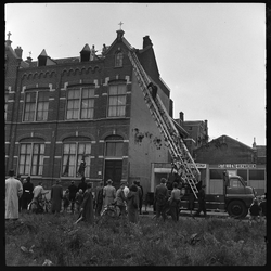 THO-1693 Een brandweerman klimt op de ladder van een brandweerwagen om een loszittende daklijst van de ...