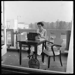 THO-1717 Tijdens de mooie nazomer werkt een vrouw op het balkon van het Groothandelsgebouw. Ze zit aan een tafel met ...