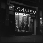 THO-1724 Avondopname van een verlichte etalage van modezaak F. Damen aan de 1e Middellandstraat 8.