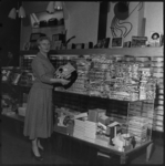 THO-1817 Mevrouw E.C. Ullersma staat met een grammofoonplaat in haar handen in een winkel van firma de Jong aan de ...