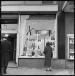 THO-1908 Een vrouw bekijkt een etalage van de Bijenkorf aan de Schiedamse Vest met tassen. In de etalage hangt een bord ...