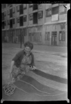 THO-194 Een vrouw klopt een mat met een mattenklopper in de Veerlaan. Op de achtergrond het voormalig magazijn van de ...