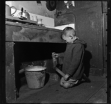 THO-1984 Een jongetje zit met een afvoerpijp in zijn handen bij een gootsteen. Onder de gootsteen staat een emmer. ...