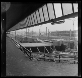 THO-3153-1 Werkzaamheden bij de bouw van het nieuwe Centraal Station. Rechts staan een locomotief en passagierstreinen.