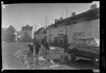 THO-85 Jongens lopen na het dooien van de sneeuw met laarzen door een modderige Damloperstraat in het Witte Dorp. Op de ...