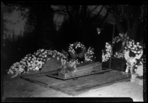 THO-928-1 Op de Algemene Begraafplaats Crooswijk wordt een kist in een graf geplaatst. Het graf is omringd door kransen ...