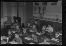 THO-936-1 Kinderen zitten met schriften achter hun tafel in een klaslokaal van de gemeenteschool aan de Jensiusstraat. ...