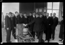 THO-965-1 Een groep mannen bekijkt een apparaat bij de opening van de Röntgen Technische Dienst (RTD) aan de Delftweg. ...