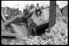 1980-5127 Puinruimers en een Nederlandse soldaat poseren op brokstukken van gewapend beton van het gebouw van de ...