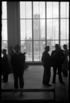 1980-5142 Een aantal mensen staan in het het Beursgebouw. Door de ramen zijn op de achtergrond de Laurenstoren en de ...
