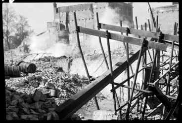 1980-5221 Rook- of stofwolken stijgen op uit restanten van verwoeste gebouwen in de Wijnstraat. Op de voorgrond liggen ...