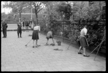 1980-5671 Vrouwen en meisjes met kortgeknipt haar moeten onkruid wieden op het pleintje voor de commandopost van de ...