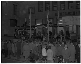 1089-04 Een kapel speelt voor het gebouw van het Rotterdamsch Nieuwsblad in verkiezingstijd. De uitslagen worden ...