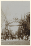XXXIII-161-2-b Mensen poseren bij een sierboog in de Erasmusstraat, tijdens de Kroningsfeesten die gehouden werden van ...