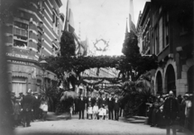 1974-1691 Leiders van het feestcomité staan op de versierde Helmersstraat, vanaf de Kruisstraat. Met links op de hoek ...
