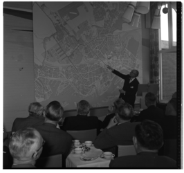 13925 Uitleg over de wederopbouw bij een grote plattegrond van het centrum in het gebouw van Gemeentewerken aan de Veemarkt.