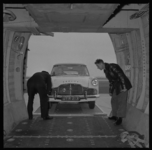 18411 Twee mannen kijken toe bij het inladen van een auto in een vliegtuig op Vliegveld Zestienhoven. Gefotografeerd ...