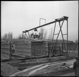 1972 Bij de bouw van noodwoningen in de Wielewaal verplaatsen bouwvakkers op het dak van een woning met behulp van een ...