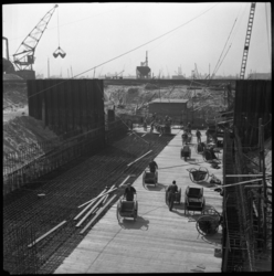 1977 Bouwvakkers lopen met kruiwagens om beton te storten op het vlechtwerk voor de bouw van de Leuvesluis. Opname ...