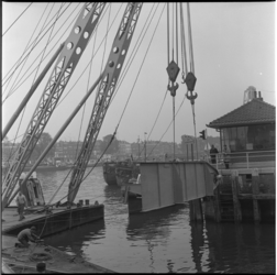 22787 Werkzaamheden aan de Binnenhavenbrug. Twee hijskranen takelen een brugelement over het water.