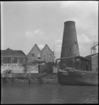 2958 Zicht op bedrijfspanden aan de Voorhaven, met rechts de molenstomp van molen 'de Distilleerketel'. Op de kade ...