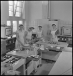 3296 Interieur van de Huishoudschool aan de Graaf Florisstraat met leerlingen in uniform in een keuken.