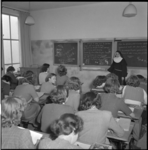 4518 Leerlingen en een docent bij het schoolbord in een klaslokaal van de Sint-Lucia Kweekschool aan de Aert van Nesstraat.