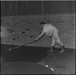 45577 Een man in een overall verft met roller een stenen ondergrond tijdens werkzaamheden voor de herinrichting van het ...