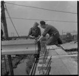 9405 Twee bouwvakkers hijsen een betonnen balk op zijn plaats bij de bouw van het Rozenviaduct over het Noorderkanaal.