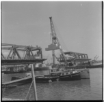 9415 De bouw van de Botlekbrug over de Oude Maas. Een contragewicht wordt met een hijskraan vanaf een schip op zijn ...