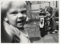 1986-2186 Man sleutelt aan zijn brommer (Zündapp). Op de voorgond een kind. Uit een serie van 10 foto's over bewoners ...