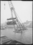 L-1153 In de Maashaven plaatst een drijvende kraan een locomotief in het ruim van een schip. De kraan wordt begeleid ...