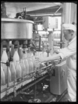 L-1283 Een medewerker staat bij een machine waarmee melkflessen worden gevuld in de Sterovita melkfabriek aan de ...