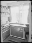 L-1476 Keuken met kookplaat, gootsteen en pannen. Onder de gootsteen staat een vuilnisemmer. Uit een serie over ...