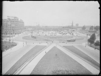 L-1575 Bussen en trams rijden op het Stationsplein. Links het Groothandelsgebouw, in het midden op de achtergrond wordt ...
