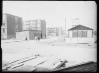 L-1856 Lage flatgebouwen aan de Schere. Langs de gebouwen staan houten keten en schuren aan opgebroken straten en ...