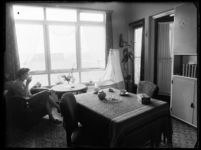 L-1866 Een vrouw drinkt thee in de woonkamer van een flatgebouw aan de Langenhorst in Zuidwijk. In het midden staat een ...