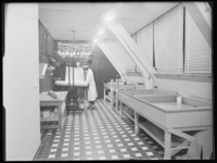 L-1874 Laborant bij een lichtinstallatie in de donkere kamer van de Fototechnische Dienst. Met de installatie wordt ...