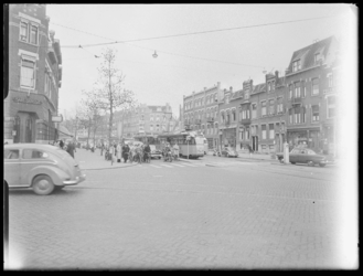 L-1900 Fietsers, auto's en een tram (lijn 4) wachten op het kruispunt 1e Midellandstraat en de 's-Gravendijkwal. Links ...